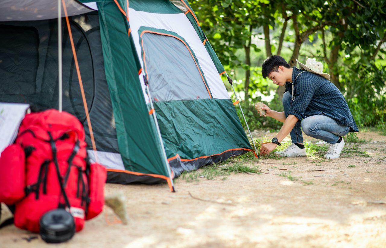 Young man pitching a tent with stones and pegs