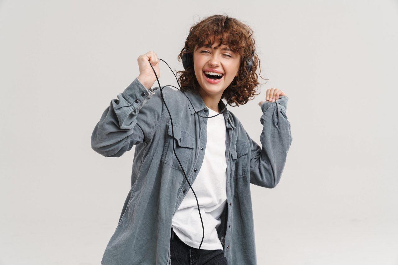 Young ginger joyful woman listening music with headphones and dancing